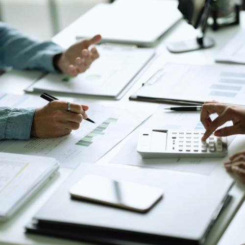 Two pairs of hands working on financial documents at a desk.